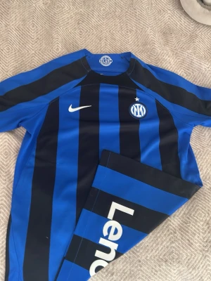 Inter Milan matchtröja Nike blå/svart - 158/170cm vilket motsvarar en xs/ m  en officiell Inter Milan matchtröja från Nike i blått och svart med klassiska vertikala ränder. Tröjan har klubbmärke, Nike-logga och Lenovo som sponsortryck. Tillverkad i lätt och funktionellt material, perfekt för fotboll eller träning. 