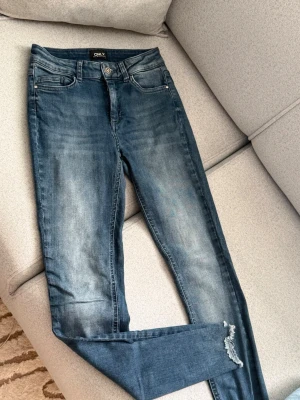 Blå skinny jeans från ONLY - Säljer ett par blå skinny jeans från ONLY med slitningar vid benslutet och snygg tvättad look. Klassisk femficksmodell med knapp och dragkedja. Jeansen är i stretchigt material för extra komfort och har en modern passform.
