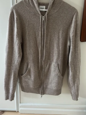 Beige hoodie i kashmir från John Henric - Mjuk och lyxig beige hoodie från John Henric i 100% kashmir. Dragkedja framtill, två fickor och ribbade muddar vid ärmslut och nederkant.  Skulle att den passar någon runt 170 cm. Mycket fint skick bortsett från lite nopprar. Kom med bud!
