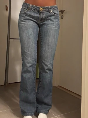 Blå bootcut jeans med låg midja - Säljer ett par klassiska blå bootcut jeans med låg midja och fem fickor. Jeansen har en snygg tvätt och stängs med gylf och knapp i guldton. Perfekta för en avslappnad och trendig look.