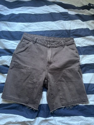 Bruna denim jorts - Zara - Säljer ett par bruna denimshorts med råa, fransiga benslut och stora fickor fram och bak. Klassisk femficksmodell med bälteshällor och knappgylf. Perfekta för en avslappnad stil.