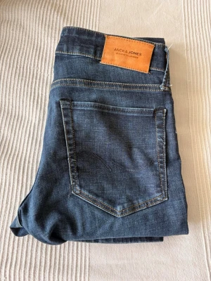 Mörkblå jeans från Jack & Jones - Snygga mörkblå jeans från Jack & Jones med klassisk femficksdesign och raka ben. Jeansen har kontrastsömmar och en läderpatch med logga bak i midjan. Perfekta till en avslappnad stil och tillverkade i mjukt denimtyg. W 28 L 30