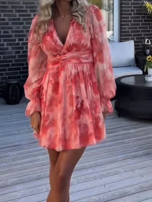 Klänning - Supersöt kort klänning med blommigt mönster i rosa och röda toner. Omlottmodell med v-ringning och långa, luftiga ärmar. Oanvänd med lappen kvar, säljer då den tyvärr är för liten för mig.💕