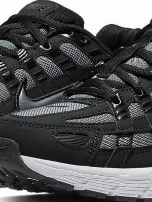 Nike svart och grå sneaker - Nike sneaker med svart och grå mesh och syntetmaterial, silverfärgad Swoosh på sidan och vit chunky sula. Skon har ett sportigt och trendigt utseende med detaljerade paneler och snörning. Perfekt för dig som gillar en clean och modern look.