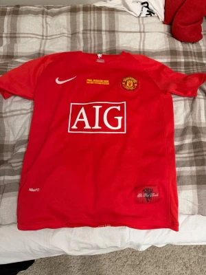 Manchester United Ronaldo tröja - Säljer en röd Manchester United matchtröja från Nike med AIG som sponsor, klubbmärke och Champions League-märke på ärmen. På ryggen står det Ronaldo och nummer 7. Tillverkad i lätt och ventilerande material, perfekt för fotboll eller träning.
