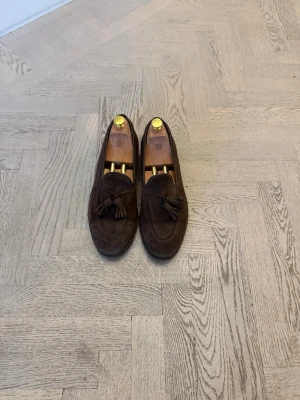 Myraqvisy: Bruna mocka loafers med tofsar - Snygga bruna loafers i mocka med klassiska tofsar framtill. Skorna har en stilren och tidlös design med rundad tå och låg klack. Perfekta för dig som gillar en dressad men avslappnad look. Nypris 3500