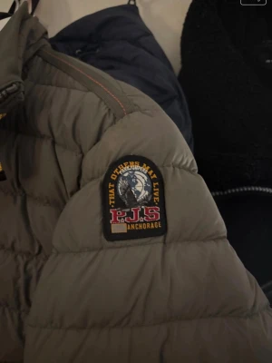 Grå dunjacka från Parajumpers - Snygg grå dunjacka från Parajumpers med patch på ärmen och orange detalj vid kragen. Jackan är lättviktig och har klassisk quiltad design. Perfekt för kalla vinterdagar och riktigt trendig stil.--