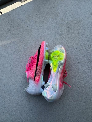 Nike Air Zoom Mercurial rosa fotbollsskor elit - Säljer ett par Nike Air Zoom Mercurial fotbollsskor i vitt och neonrosa med svarta detaljer. Skorna har en modern, strömlinjeformad design och genomskinlig sula med gula inslag. Medföljer en rosa dustbag med Nike-logga. Perfekta för dig som vill sticka ut på planen. (Den är elit)