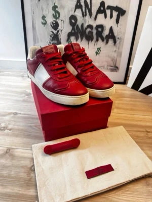 Valentino flycrew röda skor - Snygga röda och vita sneakers från Valentino Garavani i läder. Klassisk låg modell med vita detaljer på sidan och vit sula. Skorna har röda skosnören och diskret logga på plösen. Perfekta för dig som vill sticka ut med stilrena detaljer.