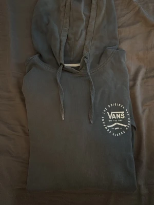 Mörkgrå hoodie från Vans - Säljer en mörkgrå hoodie från Vans med vit logga på bröstet. Hoodien har huva med dragsko och en stor magficka. Perfekt för dig som gillar streetwear och vill ha något bekvämt och snyggt. Materialet är mjukt och passar till chill dagar.