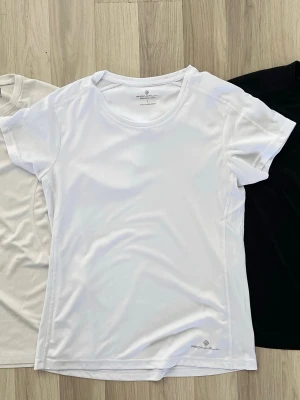 3 träningströjor - Vit t-shirt från med rund halsringning och korta ärmar. Tillverkad i ett mjukt och lätt polyestermaterial som passar perfekt för en aktiv livsstil. Diskret logga nertill på framsidan. Enkel och stilren design. 180kr totalt, 70kr styck.
