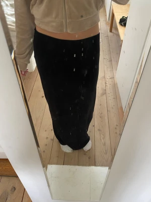 Svart långkjol i mjukt material - En svart långkjol med rak passform som sitter snyggt i midjan. Kjolen är enkel och stilren, perfekt att matcha med olika toppar. Materialet känns mjukt och följsamt mot kroppen.