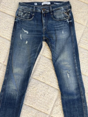 Replay anbass (aged 05 year) - Säljer ett par blå jeans från Replay med slitna detaljer och tvättade partier för en cool, avslappnad look. Klassisk femficksmodell med knappgylf och slim i passformen. OBS. NOTERA SLITAGE PÅ SISTA BILDEN