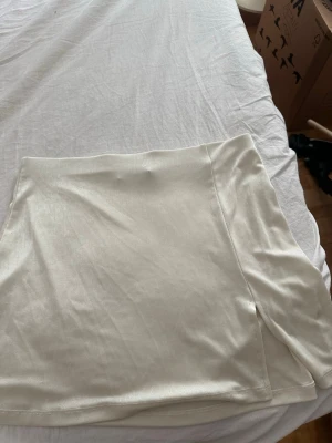 Ljusbeige kortkjol med slits - Snygg ljusbeige kortkjol i ett glansigt material med en liten slits på sidan. 