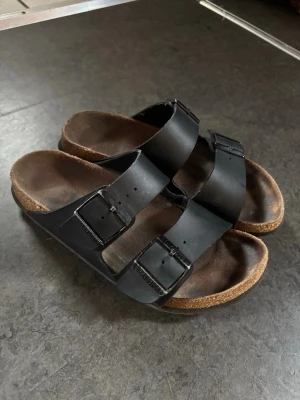 Svarta Birkenstock  - Säljer ett par jättefina Birkenstock Arizona i strl 38. Endast en liten defekt på hälen som man ser på bilden. Annars så är de super fina. Skriv om ni har några frågor 😊
