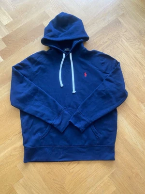 Mörkblå hoodie från Polo Ralph Lauren - Snygg mörkblå hoodie från Polo Ralph Lauren med klassisk röd logga på bröstet. Hoodien är väldigt snygg och lätt att styla. Priset är inte hugget i sten och har ni skriv om ni har några frågor!