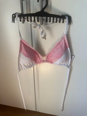 Bikinitopp från Elsa & Rose, rosa/vit. Strl L - Säljer en snygg trekantsbikinitopp från Elsa & Rose i storlek L. Toppen är vit med rosa spetsdetaljer och har knytband i nacken och ryggen. Materialet är mjukt och stretchigt, perfekt för sommaren eller stranden.