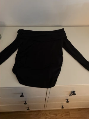 Svart offshoulder topp - Snygg svart offshoulder topp med långa ärmar. Toppen har en tight passform och är perfekt för dig som gillar en stilren look. Materialet känns mjukt och stretchigt, vilket gör den bekväm att bära.