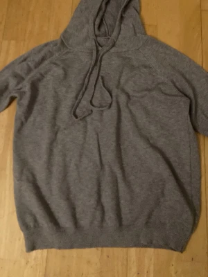 Grå hoodie med huva och dragsko - Mysig grå hoodie med huva och dragsko. Tillverkad i mjukt stickat material (cashmire/ullblandning) som känns skönt mot huden. Klassisk passform med långa ärmar och ribbade muddar vid ärmslut och nederkant. Perfekt för en avslappnad stil.