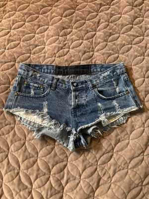 Blå jeansshorts - Snygga korta blå jeansshorts från One Teaspoon med slitna detaljer och fransig kant. Klassisk femficksmodell med låg midja och råa avslut. Perfekta för varma dagar och en avslappnad stil. Står ingen storlek men skulle säga att den är som storlek S! Pris går att diskuteras!💓