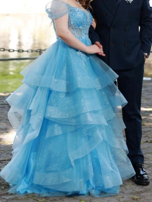 💙 Sagolik bal- förlovnings klänning från Örebro DENTELLE 💙 - Säljer min vackra ljusblå balklänning från Örebro Dentelle. Klänningen har endast använts i cirka 3 timmar och är i mycket fint skick. Klänningen har en figursydd överdel med broderier och glittrande detaljer samt flera lager tyll som ger en riktig prinsesskänsla.Off shoulder-design med romantiska ärmar.  Perfekt för: • Studentbal • Bal • Förlovning • Fest eller fotografering  Storlek:36 (upplevs rymligare och passar även något större storlek) Skick:Mycket fint skick Nypris:7000kr Pris:5000, bud