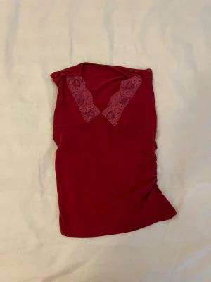 Rött nattlinne med spetsdetalj - Mörkrött nattlinne med djup V-ringning och dekorativa spetsdetaljer vid bysten. Tillverkat i ett mjukt, stretchigt material som sitter skönt mot kroppen. Nattlinnet har en figurnära passform och rynkade sidor för en snygg siluett.