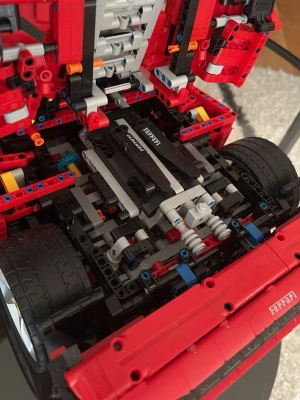 LEGO Technic Ferrari bilmodell - Detaljerad LEGO Technic bilmodell av Ferrari med röd kaross, svarta och blå detaljer samt autentiska dekaler. Modellen har synlig motor, fjädring och blå sportstolar i kupén. Perfekt för dig som gillar bilar och byggsatser.