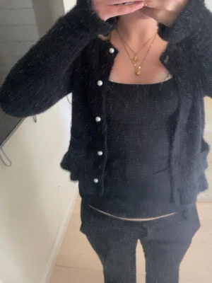 Svart kofta från Lindex - Mysig svart kofta från Lindex med fluffig textur och pärlemorknappar. Koftan har två fickor framtill och ribbade kanter vid ärmslut och nederkant. Perfekt för lager-på-lager och en chill look.
