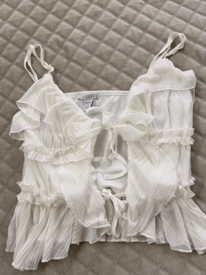 Vit volang topp från Missguided - Söt vit linnetopp från Missguided med tunna axelband, volanger och knytning fram. Toppen har ett skirt, lätt plisserat tyg och romantiska detaljer som ger en luftig känsla. Perfekt för dig som gillar en feminin och trendig stil.
