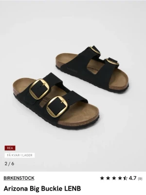Birkenstock Arizona Big Buckle sandaler - Svarta Birkenstock Arizona Big Buckle sandaler med två breda remmar i mocka och stora guldfärgade spännen. Fotbädden är i kork och mocka för extra komfort. Klassisk slip-in modell med svart yttersula och stilren design.