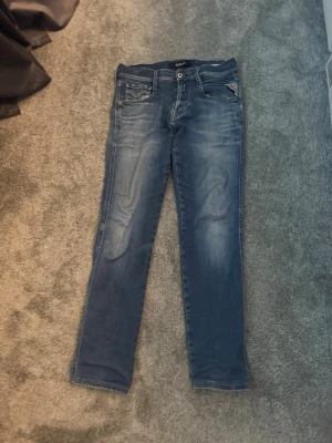 Blå slim fit jeans från replay (andbass) - Säljer ett par blå slim fit jeans från replay med klassisk femficksdesign och snygga slitningar framtill. Jeansen har normal midja och raka ben, tillverkade i mjuk denim med lite stretch för extra komfort. Perfekta till vardagslooken!