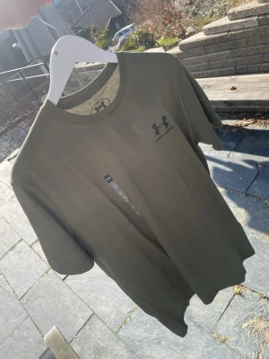 Olivgrön t-shirt från Under Armour - Snygg olivgrön t-shirt från Under Armour med diskret logga på bröstet. Klassisk rund halsringning och korta ärmar. Den är helt ny med lapp på, endast prövad och då var den för stor!