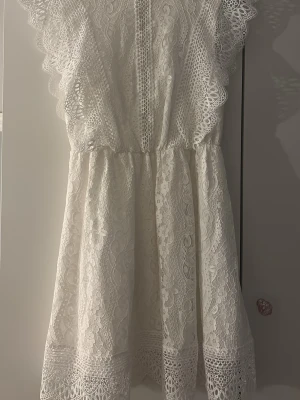 Vit spetsklänning med volang - Helt oanvänd Superfin vit kortklänning i spets med v-ringning och breda volangdetaljer längs axlarna. Klänningen har ett vackert spetsmönster och markerad midja, perfekt för Konfirmation eller student klänning❣️pris kan diskuteras och nypris är 499kr🌸