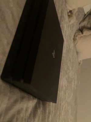 PlayStation 4 Pro svart konsol 1TB - Säljer en svart PlayStation 4 Pro 1TB från Sony. Konsolen har en stilren, matt finish och den klassiska PS-loggan på ovansidan. Den har en kantig, rektangulär form med tre lager och är tillverkad i plast. Perfekt för gaming och streaming.