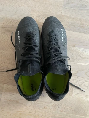 snygga svarta Nike Air Zoom fotbollsskor - Svarta Nike Air Zoom fotbollsskor med snörning och hög krage för extra stöd. Skorna har en modern design med vita detaljer och logga, samt grön innersula och dobbar för bra grepp på planen. Tillverkade i syntetmaterial som ger lätt  känsla och bra bollkontroll.