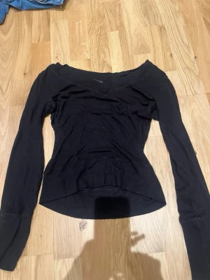 Svart långärmad topp från H&M - Snygg svart långärmad topp från H&M med lång ärm och ribbad struktur. Toppen har en bred urringning som sitter snyggt över axlarna och är lätt croppad framtill. Perfekt att styla med jeans eller kjol för en trendig look.