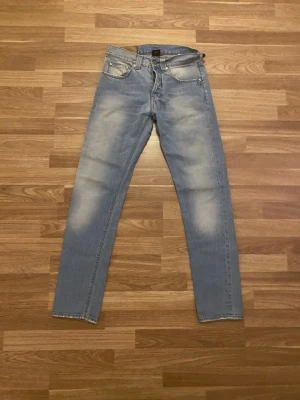 Ljusblå raka jeans med slitningar - Säljer ett par ljusblå jeans med raka ben och snygga slitningar på låren och knäna. Jeansen har klassisk femficksdesign och normal midja. Perfekta för en avslappnad och trendig look.