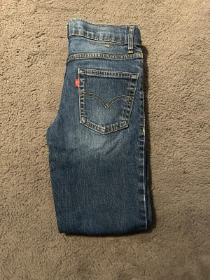 Levi's blå raka jeans - Klassiska blå jeans från Levi's med raka ben och tydliga kontrastsömmar. Jeansen har en bakficka med den ikoniska V-formade sömmen och röd Levi's-tag. Tillverkade i slitstark denim som ger en tidlös look.