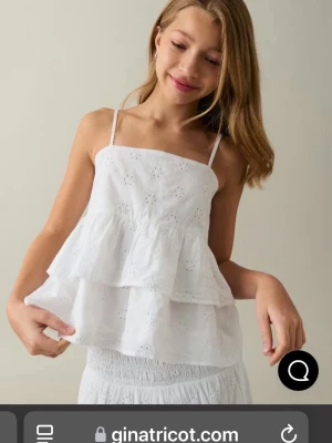 Vit volangtop från Gina Tricot - Söt vit linnetopp med tunna axelband och dubbla volanger. Toppen har broderade blommor och ger en luftig känsla, perfekt för varma dagar. Styla med jeans eller kjol för en fräsch look. Är i barnstorlek men passar mig som har xs. Skriv för exakta storlek. Orginalpris 250 knappt använd