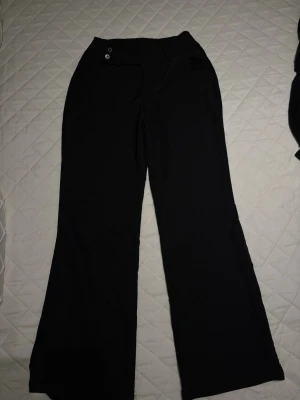 Svarta vida kostymbyxor - Snygga svarta kostymbyxor med vida ben och hög midja. Byxorna har två knappar i midjan, bälteshällor och fuskfickor bak. Perfekta för en stilren look och passar till många olika outfits.