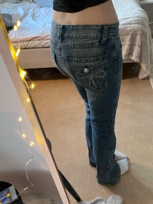 Blå bootcut jeans med detaljer - De har förlorat en knapp på en av fickorna och är pyttelite slitna längst ner på benen. De är jättefina paljetter på fickorna där bak och tycker jeansen är sjukt snygga men dom är för små för mig och har tappat bort kvittot!💕
