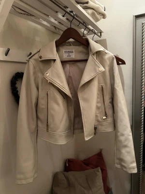 Krämvit skinnjacka från & Other Stories - Snygg krämvit skinnjacka från Ullared med klassisk bikerdesign, bred krage och guldfärgade dragkedjor. Jackan har två fickor framtill och axelklaffar för extra detaljer. Perfekt för dig som vill ha en stilren och trendig look. Nypris 500kr Använd endast 2 gånger! Skriv vid frågor eller intresse💗Köpare står för frakt 