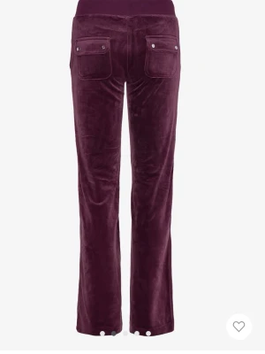 Vinröda velourbyxor Juicy Couture - Mysiga vinröda mjukisbyxor från Juicy Couture i mjuk velour. Byxorna har raka ben, bred resårmidja med dragsko och stora fickor både fram och bak. Perfekta för chill dagar och har en klassisk Juicy-look.