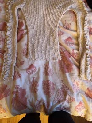 Beige ribbad stickad tröja Index - Supersöt beige stickad tröja från Index i storlek XS. Tröjan har ribbad struktur och långa ärmar med volangdetaljer längs sidorna. Perfekt för dig som gillar en feminin och trendig look. Mjuk och skön kvalitet.