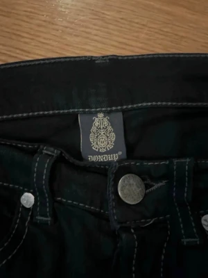 Svarta jeans från Dondup - grå och svarta - Säljer ett par svarta jeans från Dondup med kontrastsömmar och klassisk femficksmodell. Jeansen har metallknapp och nitar samt detaljerade sömmar. Tillverkade i Italien och har en snygg, tidlös look som passar till det mesta.