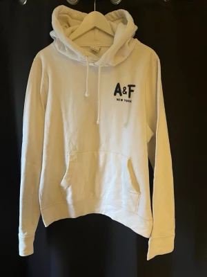 Abercrombie & Fitch hoodie vit - Tja säljer en Snygg vit hoodie från Abercrombie & Fitch med svart A&F New York-tryck på bröstet. Klassisk känguruficka framtill, dragsko i huvan och mjukt material som känns skönt mot huden. Perfekt för en avslappnad och stilren archive/laidback look. Skicket är 9/10 ungefär helt ny🤗storlek L killen på bilden är 183 och ganska smal är lite för stor för han🤩har du några frågor eller funderingar är de bara att höra av sig🙌🏼mvh premium fashion😁