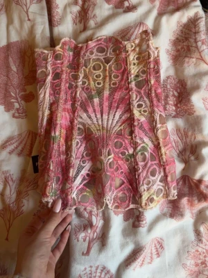 Färgglad spetskorsett med mönster - Säljer en unik korsett i spets med färgstarkt mönster i rosa, beige och grönt. Korsetten har genomskinliga partier och dekorativa sömmar som ger en cool och trendig look. Perfekt för dig som vill sticka ut och addera något extra till din outfit. Tappat två knappar men det går att fixa💕
