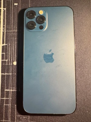 Blå iPhone 12 Pro med trippelkamera - Snygg blå iPhone 12 Pro med stilren design och trippelkamera på baksidan. Telefonen har en matt glasbaksida och ram i metall. Den ikoniska Apple-loggan syns tydligt på baksidan och framsidan har en stor skärm med tunna kanter.