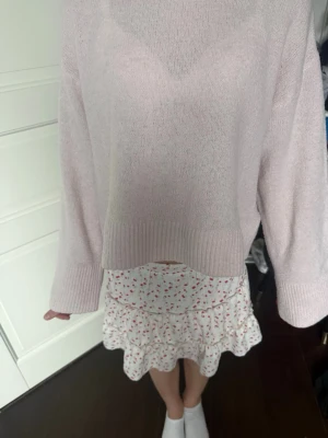 Ljusrosa stickad tröja med bred mudd - Söt ljusrosa stickad tröja med bred ribbad mudd vid ärmslut och nederkant. Tröjan har en avslappnad passform och rund halsringning. Perfekt att matcha med kjol eller jeans för en trendig look.