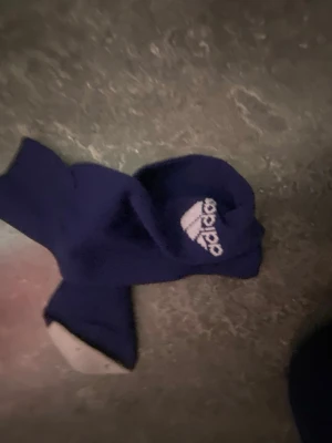 Blå Adidas strumpor med logga - Säljer ett par blå strumpor från Adidas med den klassiska vita loggan vid ankeln. Strumporna är i en sportig modell och passar perfekt till sneakers. Materialet känns mjukt och stretchigt, troligen bomullsmix.